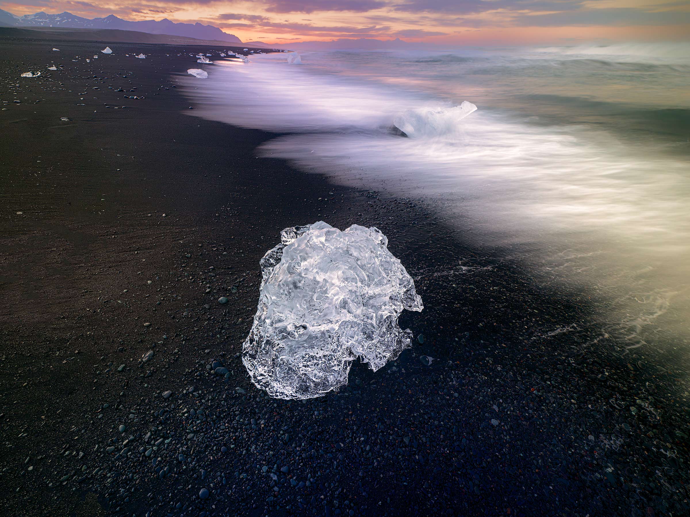 Where Fire Meets Ice A solitary fragment of glacial ice rests on the volcanic black sands of Diamond Beach as the first light of dawn paints the Icelandic...